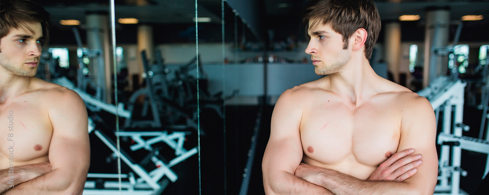 Ein junger Mann betrachtet sein Spiegelbild in einem Fitnessstudio