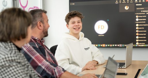 Zwei Erwachsene und ein Junge sitzen mit ihren Laptops am Tisch.