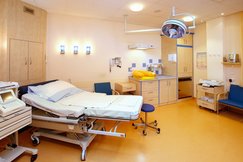 Gebärzimmer mit Gebärbett. Weiße Bettwäsche. CTG Gerät. Wärmestrahler. Babywaage. Wickelplatz. Waschplatz. große Lampe.