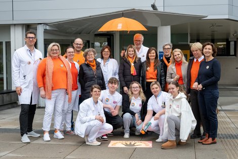 Gruppenfoto mit orangenem Schirm und orange Hände werden auf Boden gesprüht