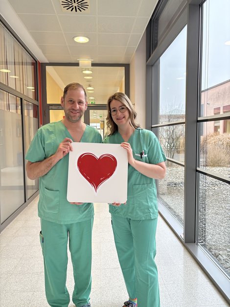 Mann und Frau in OP-Kleidung halten Herz-Bild gemeinsam vor sich