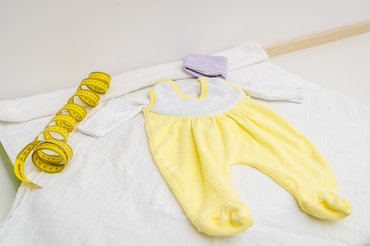 gelbes Maßband und weiß-gelber Babystrampler