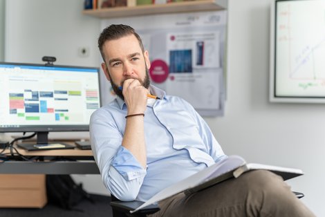 Stephan Famler sitzt in einem Büro auf einem Drehstuhl und betrachtet Unterlagen.