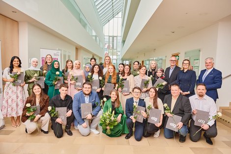 Gruppenfoto AbsolventInnen mit Gratulanten mit Diplom und Rosen in der Hand