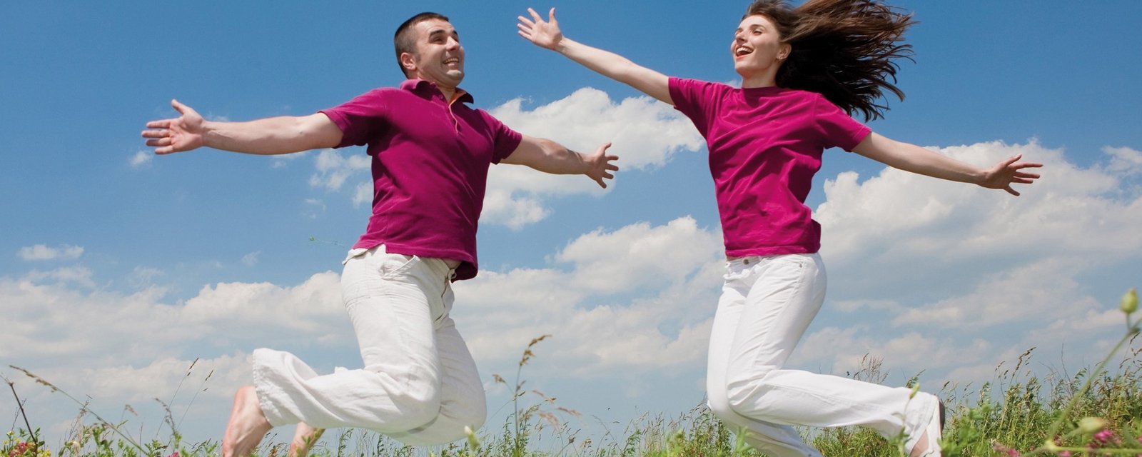 Zwei Personen springen auf einer grünen Wiese in die Luft.