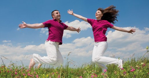 Zwei Personen springen auf einer grünen Wiese in die Luft.