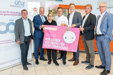 Sechs Männer und eine Frau stehen nebeneinander und halten ein rosa Transparten mit der Aufschrift "Wir haben nix übrig für Verschwendung".