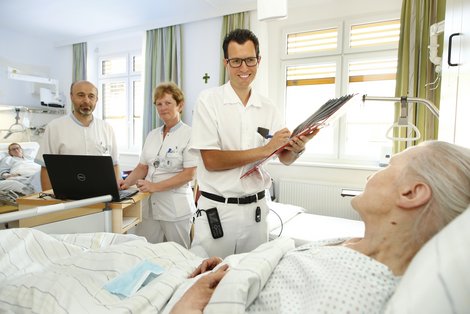 ÄrztInnen und eine Pflegekraft stehen am PatientInnenbett bei der Visite. 