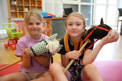Zwei Kinder spielen während der Sommerkinderbetreuung im Salzkammergut Klinikum Bad Ischl mit Steckenpferden in einem Spielraum.