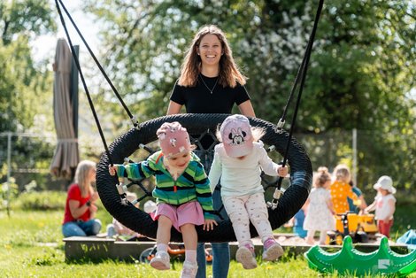 Betreuerin schubst Kinder auf der Nestschaukel an