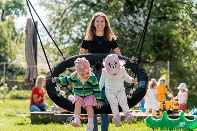 Betreuerin schubst Kinder auf der Nestschaukel an