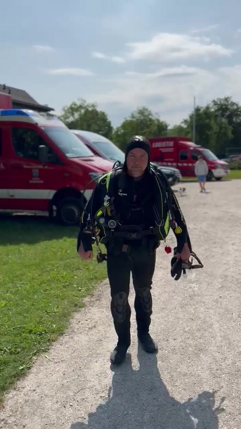 Florian Kirchmayr in kompletter Tauchausrüstung auf einem Schotterweg vor mehreren Einsatzfahrzeugen.