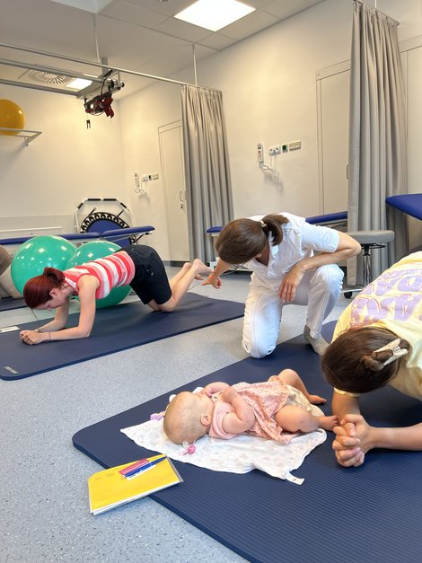 Frischgebackene Mütter machen Übungen zur Rückbildung auf Turnmatten und werden dabei angeleitet