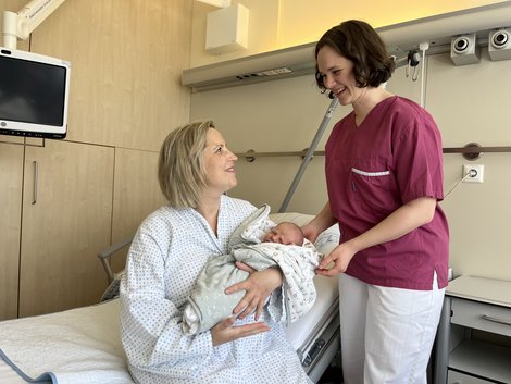 Mama mit Baby im Arm und Hebamme daneben