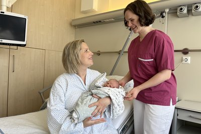 Mama mit Baby im Arm und Hebamme daneben
