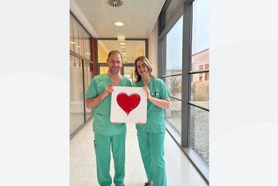 Mann und Frau in OP-Kleidung halten Herz-Bild gemeinsam vor sich