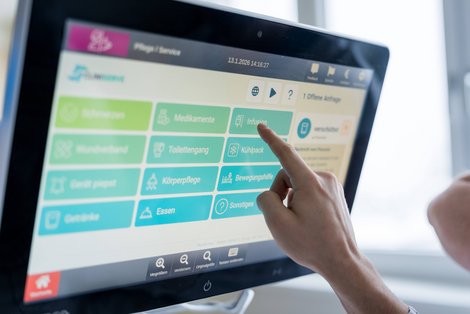 PatientIn tippt auf Bildschirm am Krankenbett