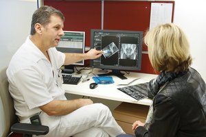 Arzt und Patientin vor einem Bildschirm mit Röntgenbild der Hüfte