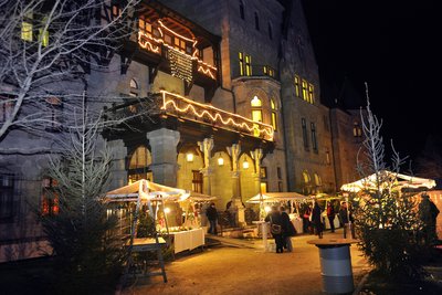 ein adventlich beleuchtetes und geschmücktes Schloss mit Ständen davor; es ist finster