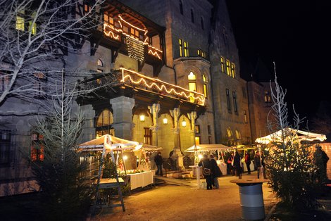 ein adventlich beleuchtetes und geschmücktes Schloss mit Ständen davor; es ist finster
