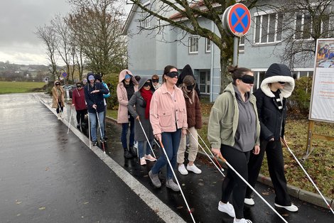 Auszubildende mit Blindenstock und Augenbinde vor der Schule