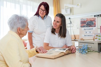Zwei Pflegekräfte sprechen mit einer alten Dame