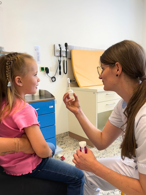 Krankenpflegerin hält Mädchen Seifenblasen-Stäbchen hin zum Durchblasen