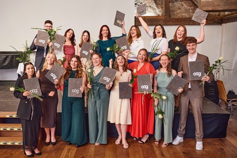 Gruppenfoto, AbsolventInnen halten Diplom und Rose in den Händen und jubeln