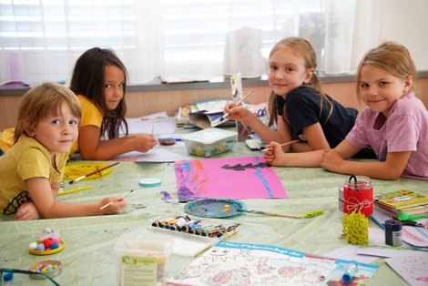 Mehrere Kinder gestalten bei der Sommerkinderbetreuung im Salzkammergut Klinikum Bad Ischl gemeinsam bunte Bilder mit Farben und Bastelmaterialien.