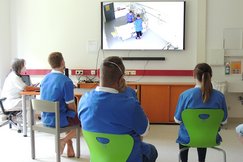 Auszubildende beobachten am Bildschirm ihre KollegInnen am Simulator im Nebenraum