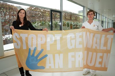 Zwei Mitarbeiterinnen halten ein Transparent hoch: "Stopp Gewalt an Frauen"