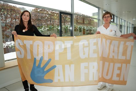 Zwei Mitarbeiterinnen halten ein Transparent hoch: "Stopp Gewalt an Frauen"