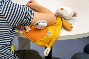 Oberarm eines Kindes mit Blutzuckersensor darunter Kuscheltier