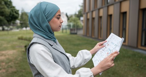 Lehrling zur Bautechnische Zeichnerin steht mit einem Plan vor einem Gebäude