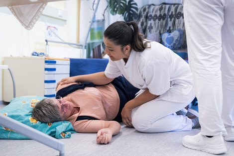 Schauspielpatient liegt am Boden, Auszubildende übt stabile Seitenlage