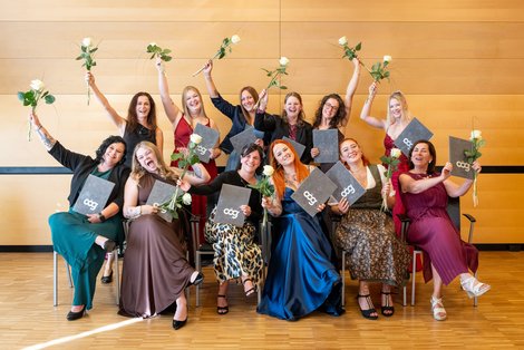 Gruppenfoto jubelnder Absolventinnen mit ihren Diplomen und einer Blume in der Hand
