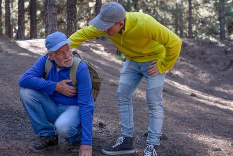 Älterer Mann hält sich beim Wandern die Brust, jüngerer kümmert sich
