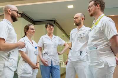 Drei Ärzte und2 Ärztinnen in Dienstkleidung stehen im Halbkreis in einem Gang nebeneinander.