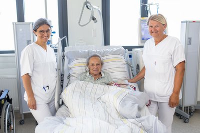 DGKP Christa Garstenauer und DGKP Andrea Hofstätter stehen am Patientenbett einer Dialysepatientin