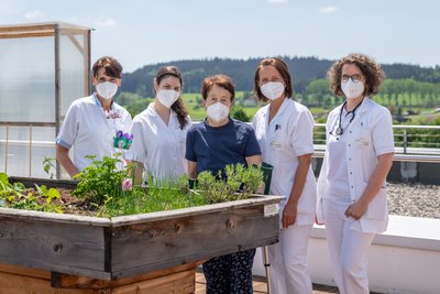 Das Team der Akutgeriatrie und Remobilisation des Klinikums Rohrbach auf der Terrasse der Klinikums, wo gemeinsam mit PatientInnen wie Christine Atzgerstorfer Hochbeete bepflanzt, gehegt und gepflegt werden. 