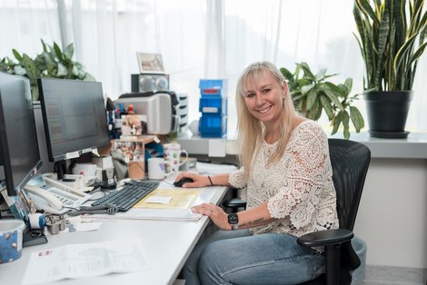 Sylvia Hollnsteiner an ihrem Arbeitsplatz im Büro schaut lächelnd in die Kamera