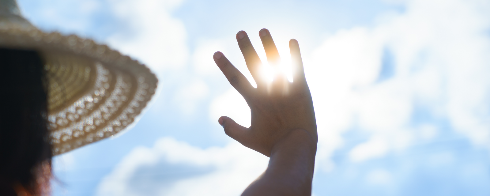 Frau mit Sonnenhut hält Hand gegen die Sonne