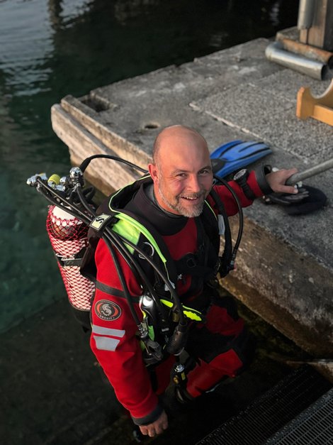 Florian Kirchmayr in vollständiger Tauchausrüstung auf einer Treppe im Wasser neben einem Betonsteg.