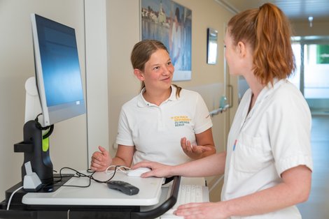 Zwei Pflegeschülerinnen stehen bei Visitenwagen und unterhalten sich