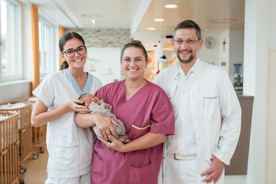 Primar, Pflegekraft und Hebamme mit Baby im Arm