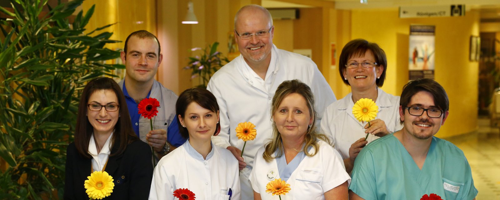 4 Mitarbeiterinnen und 3 Mitarbeiter mit Blumen in der Hand
