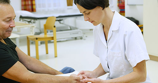 Mitarbeiterin der Ergotherapie trainiert mit Patient die Hand