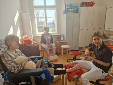 Mitarbeiterin macht Fußpflege bei Bewohnerin - im Hintergrund sitzt andere Bewohnerin und genießt Fußbad