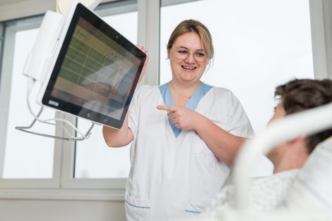 Pflegemitarbeiterin erklärt Patient Kommunikation über Bildschirm am Krankenbett