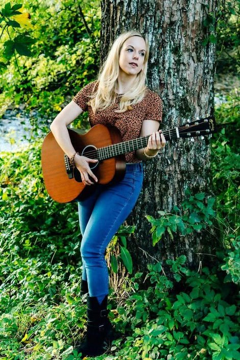 Andrea Nußbaumer lehnt an einem Baum und spielt Gitarre